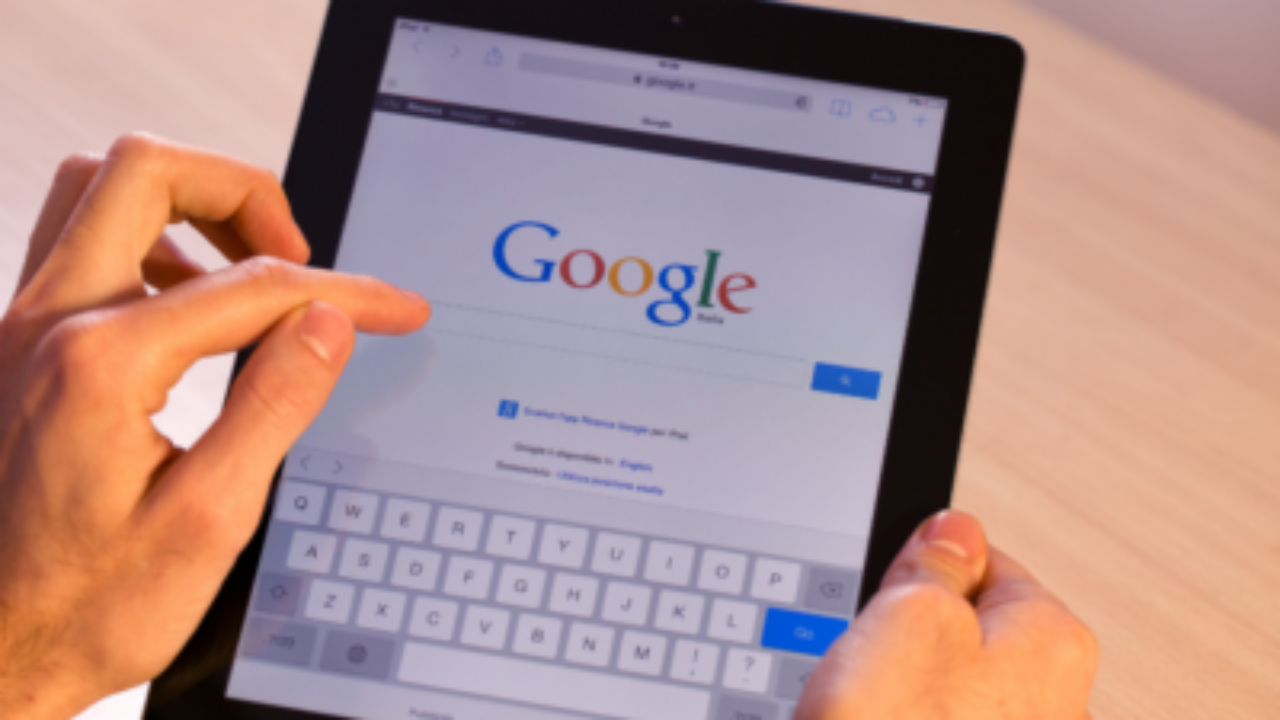 “Hands holding a tablet while typing in the Google search bar on the screen