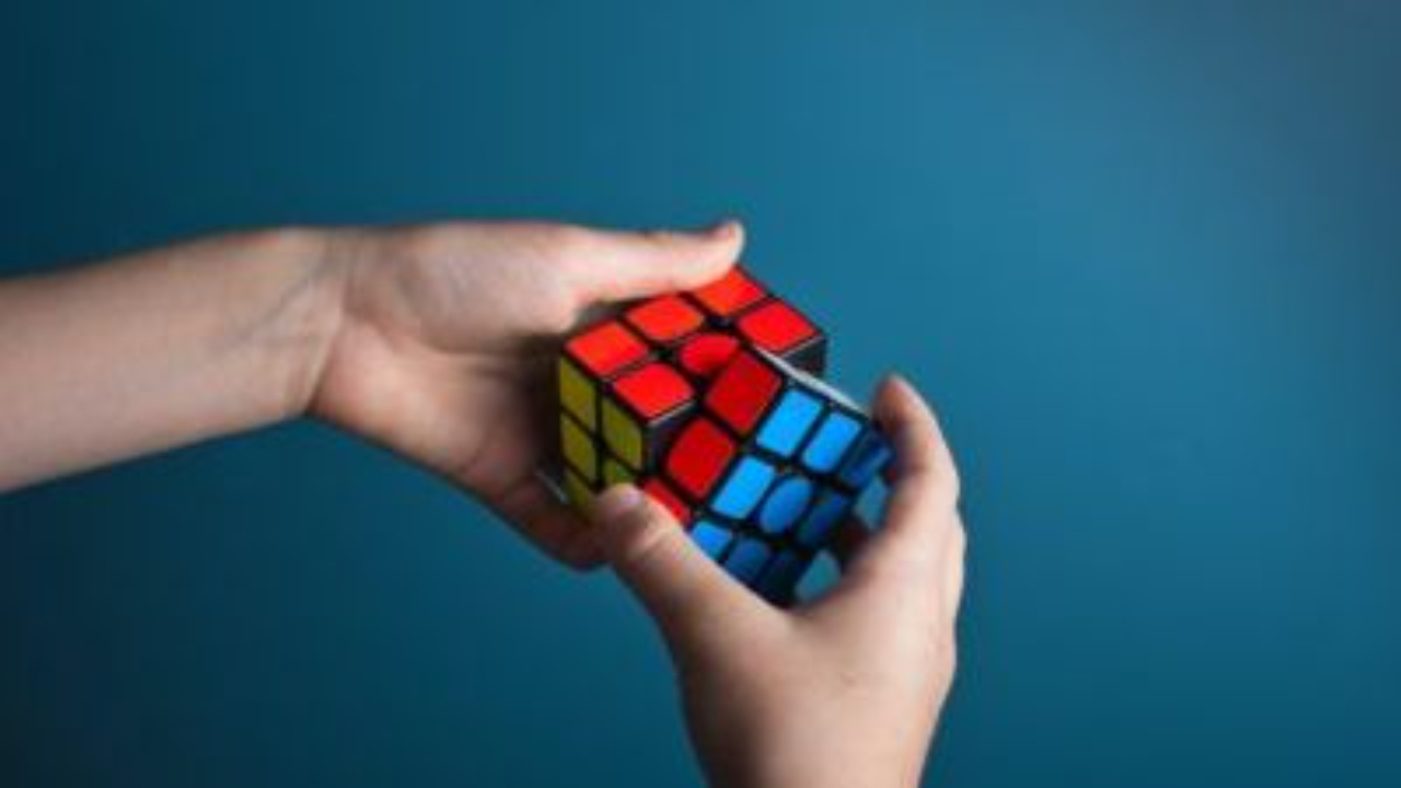 Hands holding and twisting a colorful Rubik’s Cube against a blue background