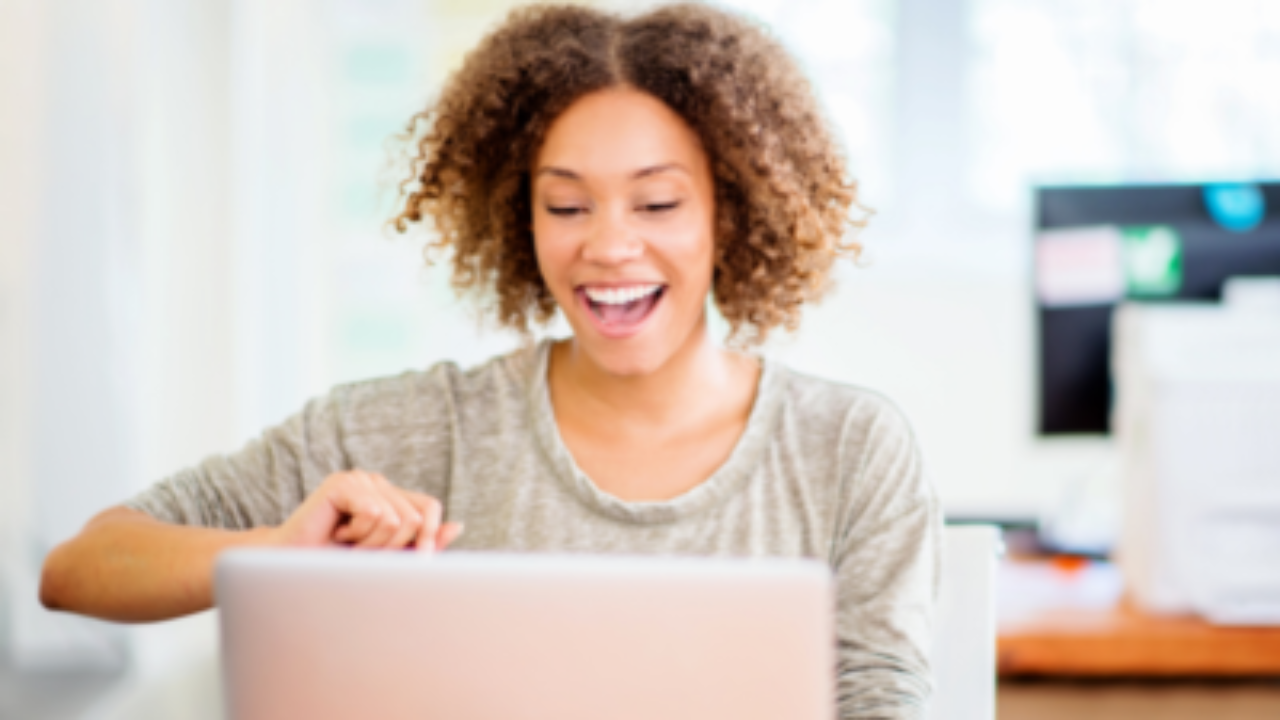Woman smiling while working on a laptop in a bright office