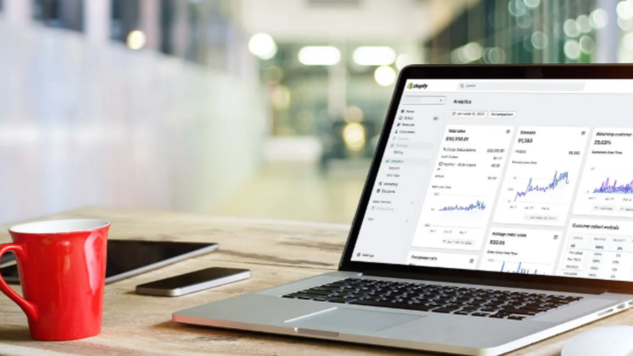 Laptop displaying Shopify analytics dashboard on a desk with a coffee mug, representing ecommerce store data and performance tracking.