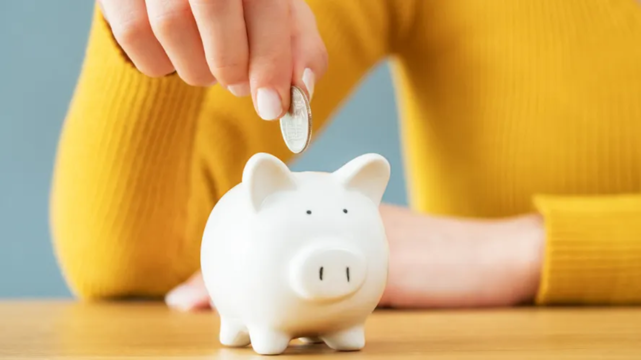 A hand dropping a coin into a white piggy bank, symbolizing paying yourself from your ecommerce business.