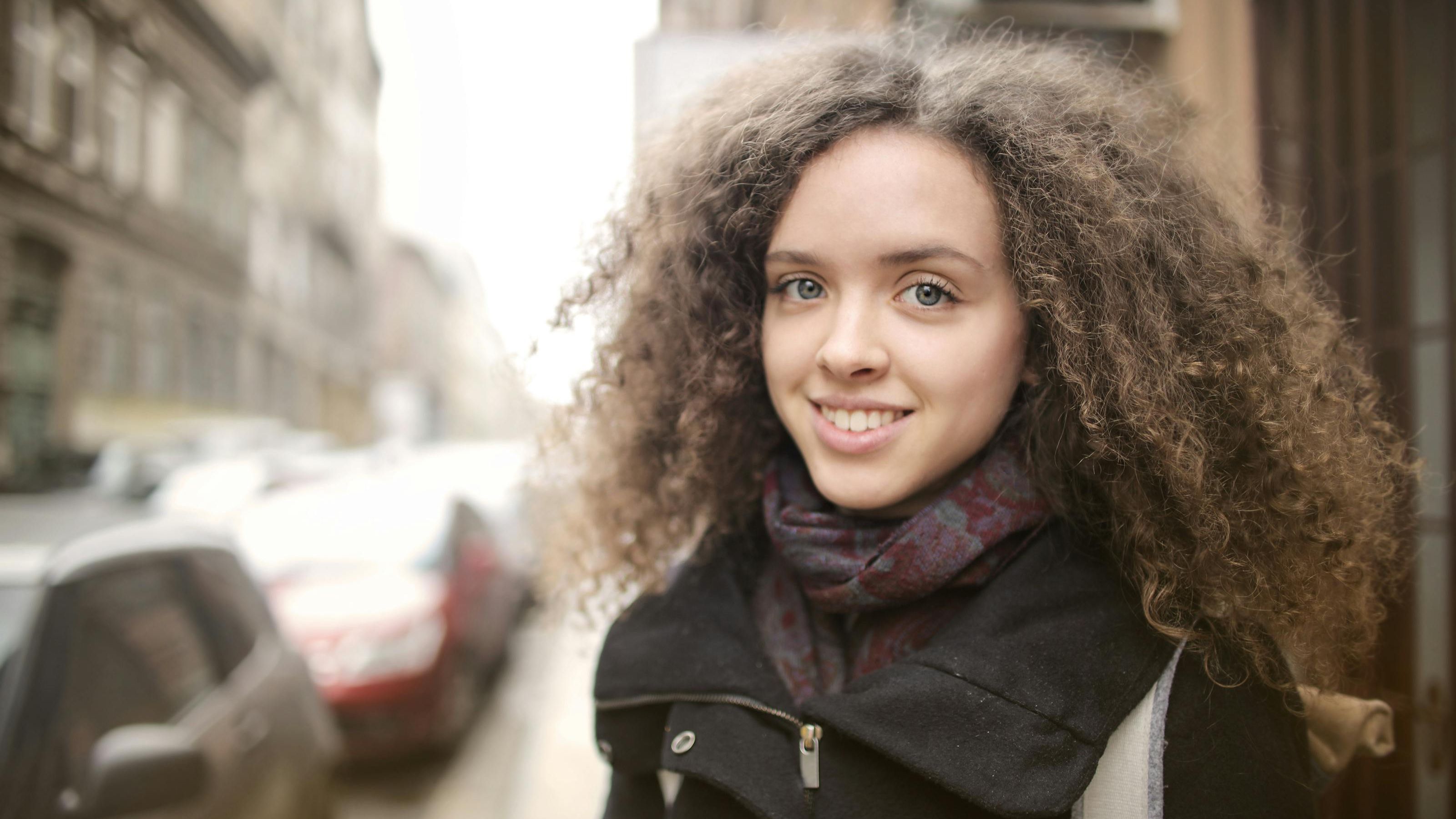 A confident young woman smiling softly on a city street, symbolizing self-trust, inner confidence, and emotional growth.