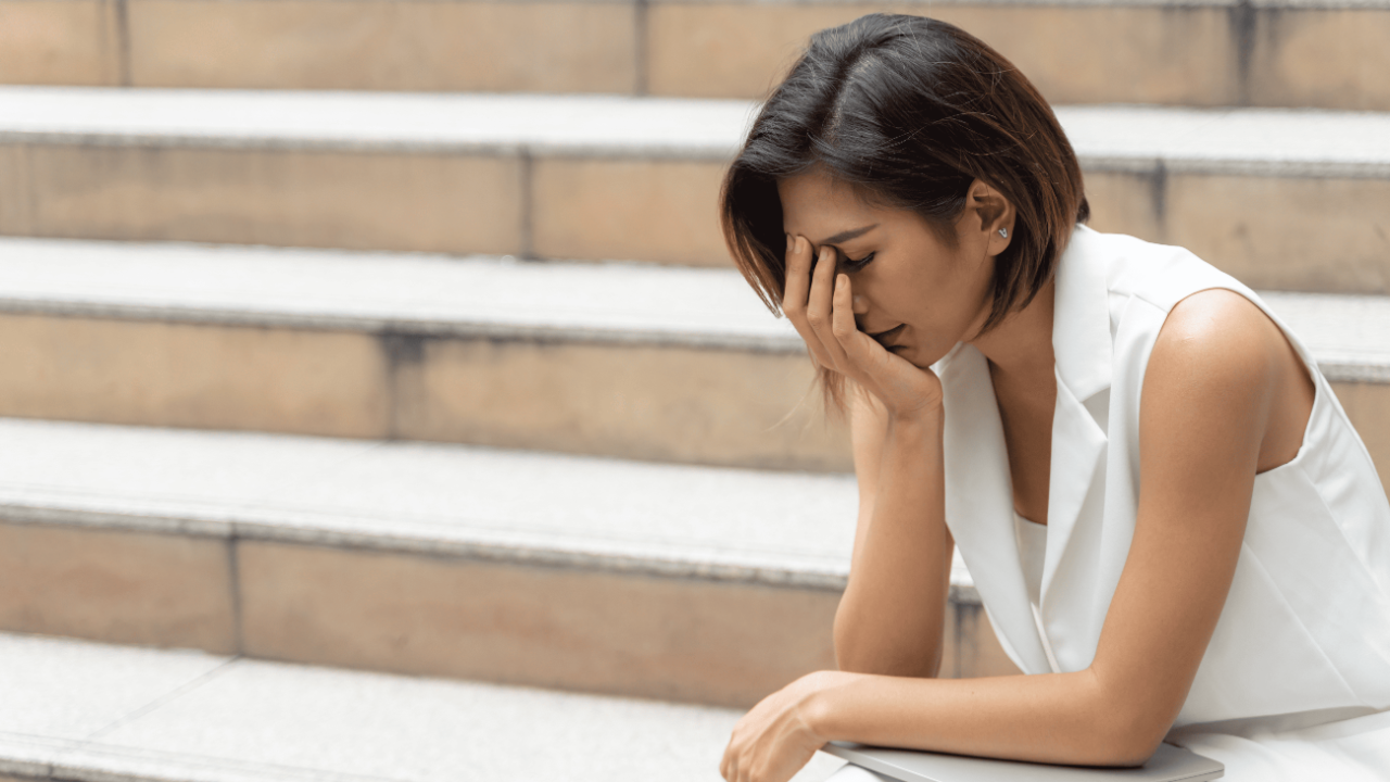 Distressed woman sitting on stairs with head in hand, representing emotional exhaustion from toxic relationships and weak personal boundaries.