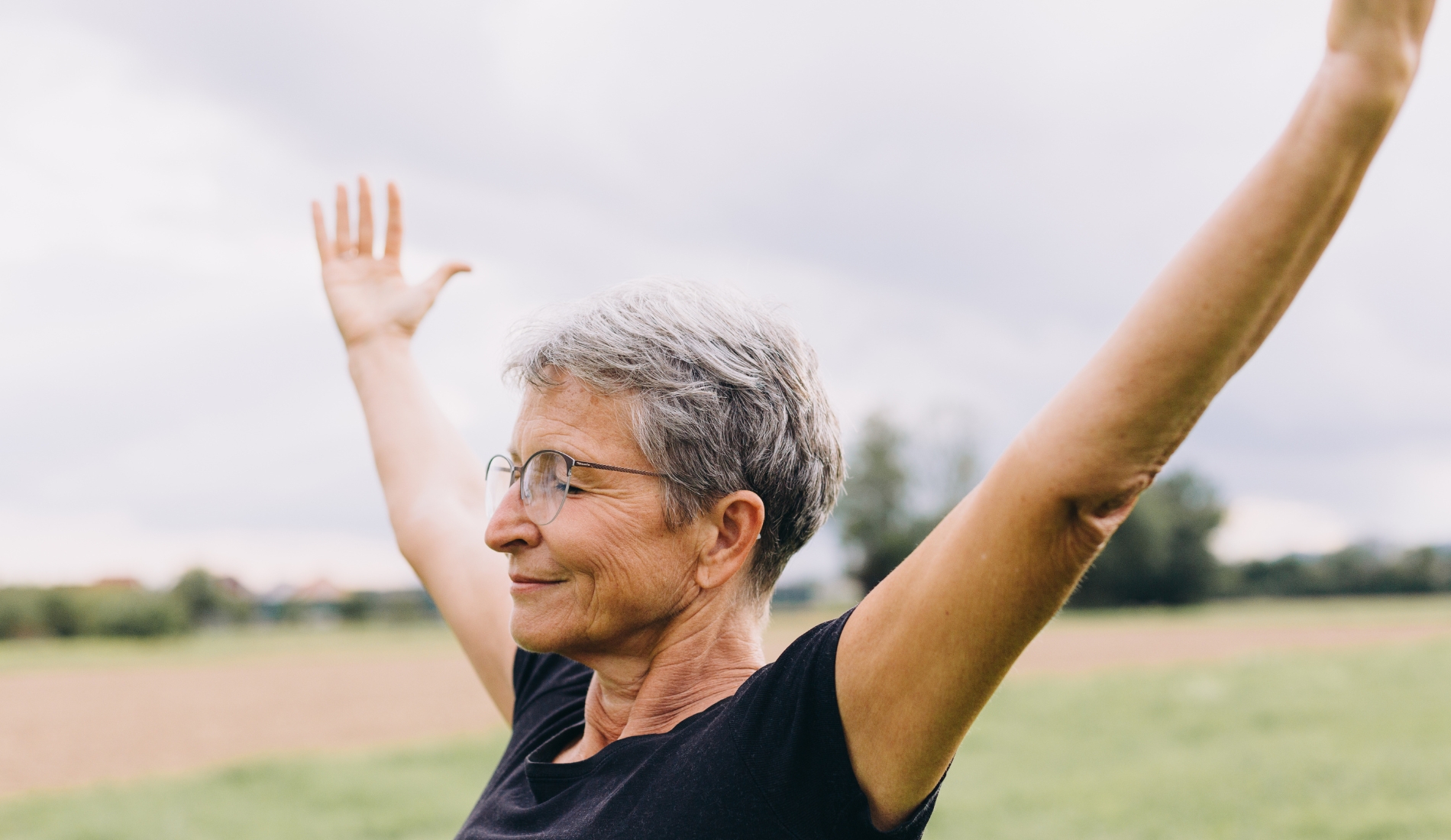 Smiling older woman with gray hair raising her arms outdoors, feeling strong and confident