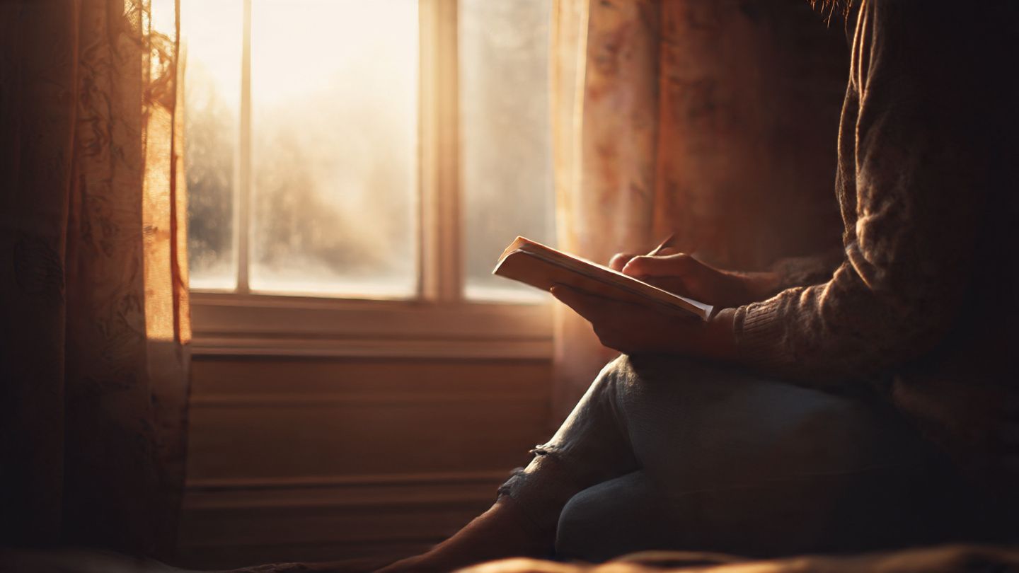 Person journaling in quiet reflection by a window, representing forgiveness and freedom in faith.