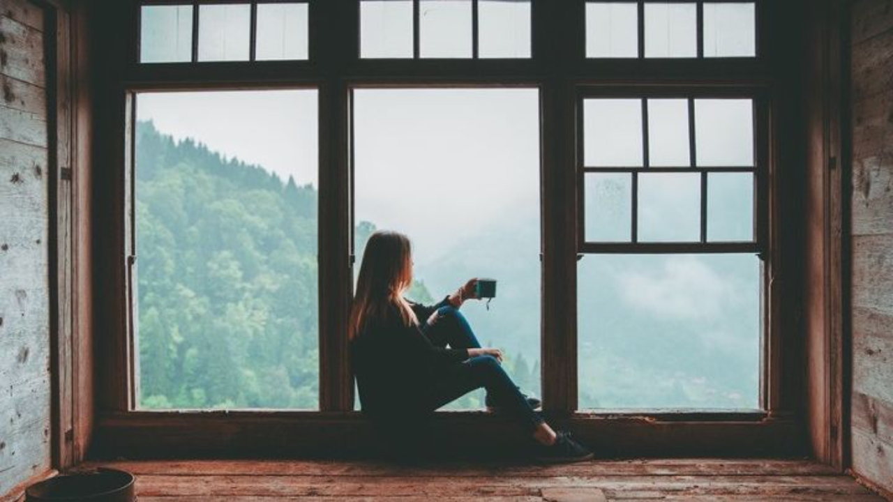 reflective image of midlife women looking out a window onto forest and mountains 