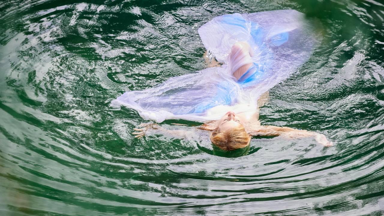 Woman standing by ocean with eyWoman floating on her back with arms open, symbolizing surrender, trust, and alignment with flow.