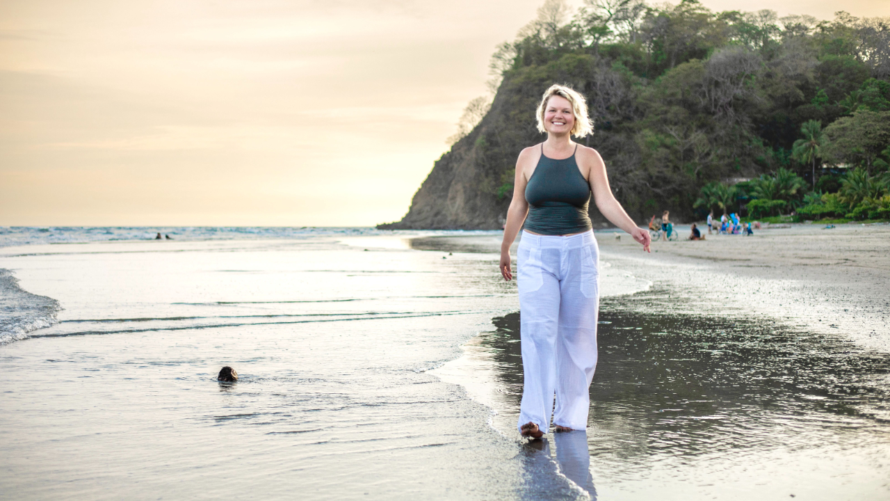 Woman walking along a sunlit shore, symbolizing trust in the journey and following intuitive nudges.
