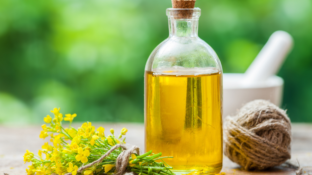 a bottle of canola oil on a table outdoors sitting next to a bundle of flowers and a ball of hemp with a mortar and pestle in the background