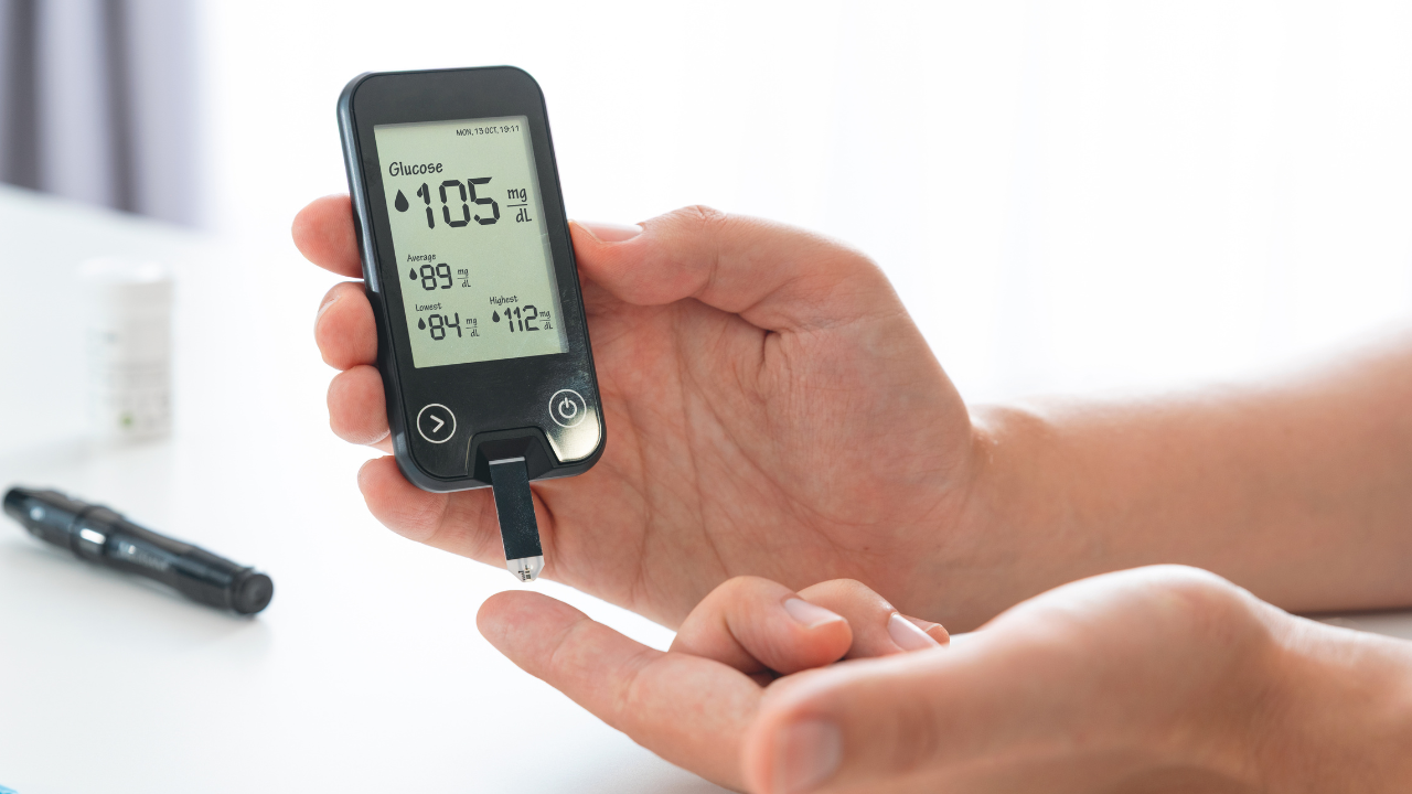 two hands using a glucometer to read blood sugar showing 105mg per deciliter