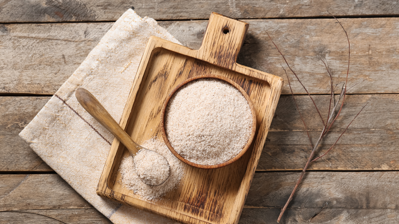 psyllium husk in a bowl and spoon on a wooden tray on a wooden table with a branch next to it