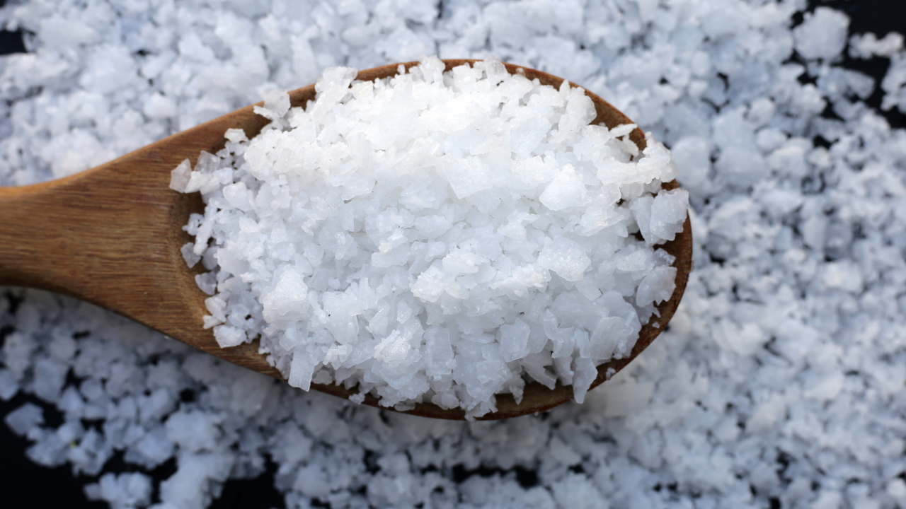a wooden spoon filled with flakes of table salt, surrounded by a background of table salt