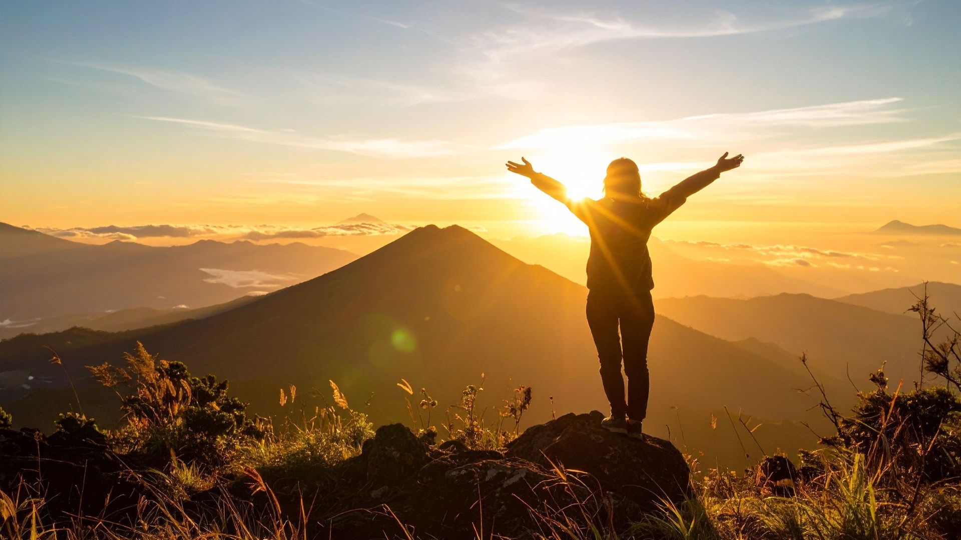 Silhouette of a man standing on a mountain peak at sunrise, looking out over a vast landscape symbolizing new hopes, big dreams, and future possibilities.