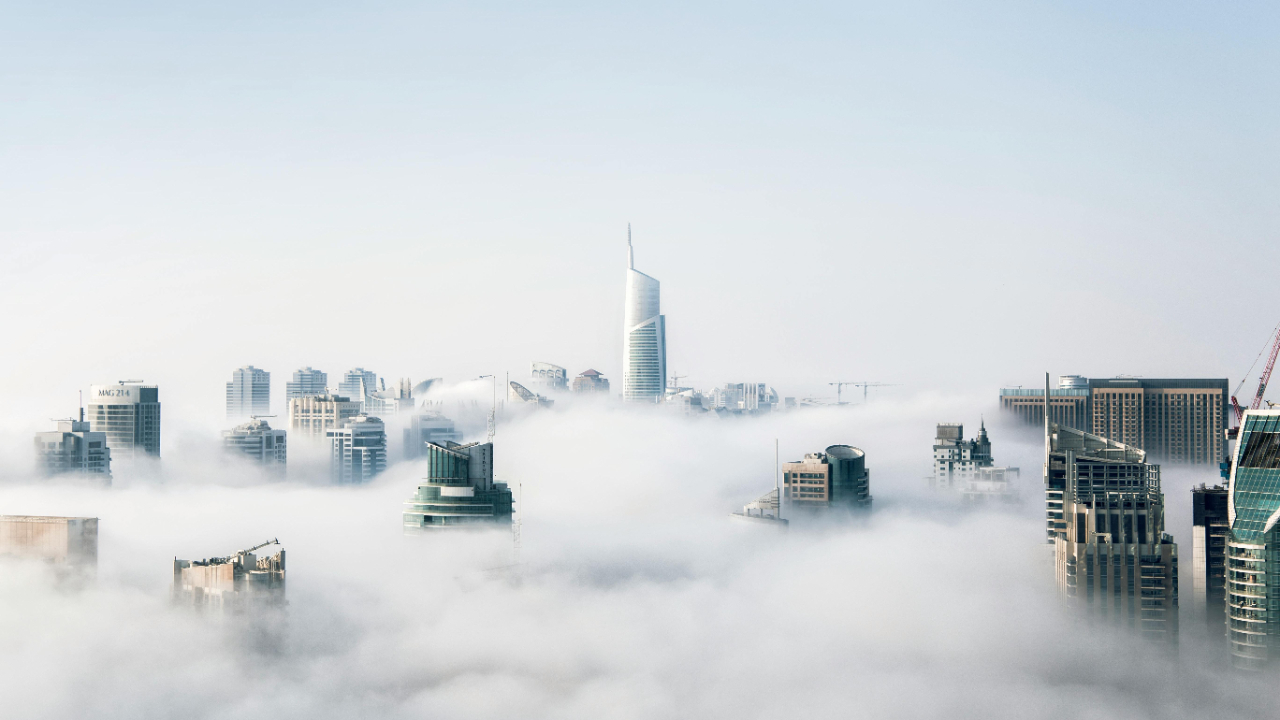 A city skyline with tall modern buildings emerging through low clouds and fog.