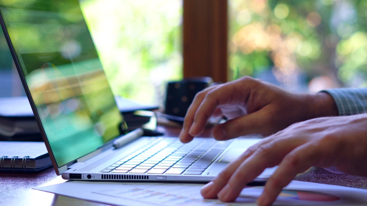 Person typing on a laptop with paperwork nearby, symbolizing ICF credential renewal and organizing CCE hours