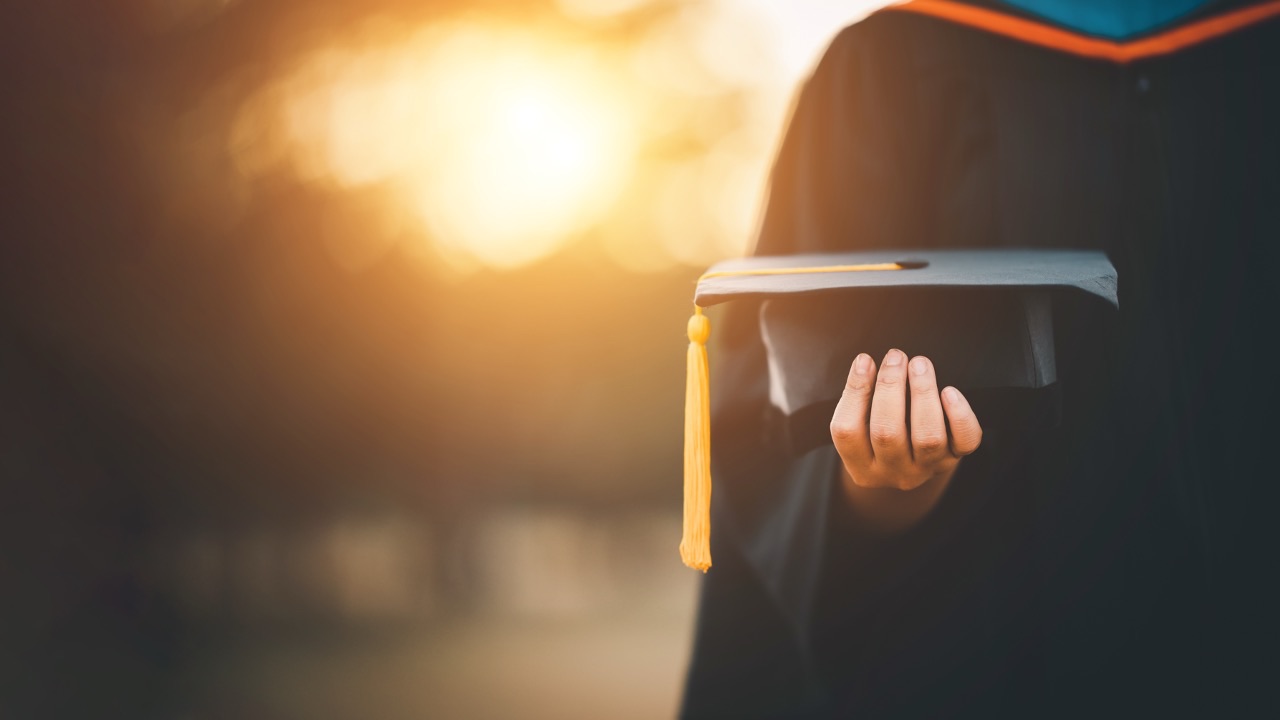 PhD graduate holding a mortarboard cap, representing evidence-based wellbeing coaching, doctoral academic research, and professional coaching development