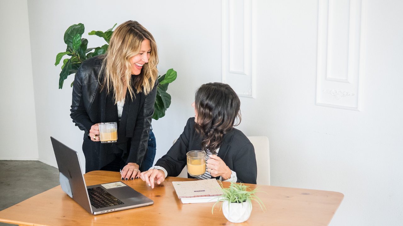 Bride and groom laughing over coffee while planning their wedding on a laptop using a digital planning guide.