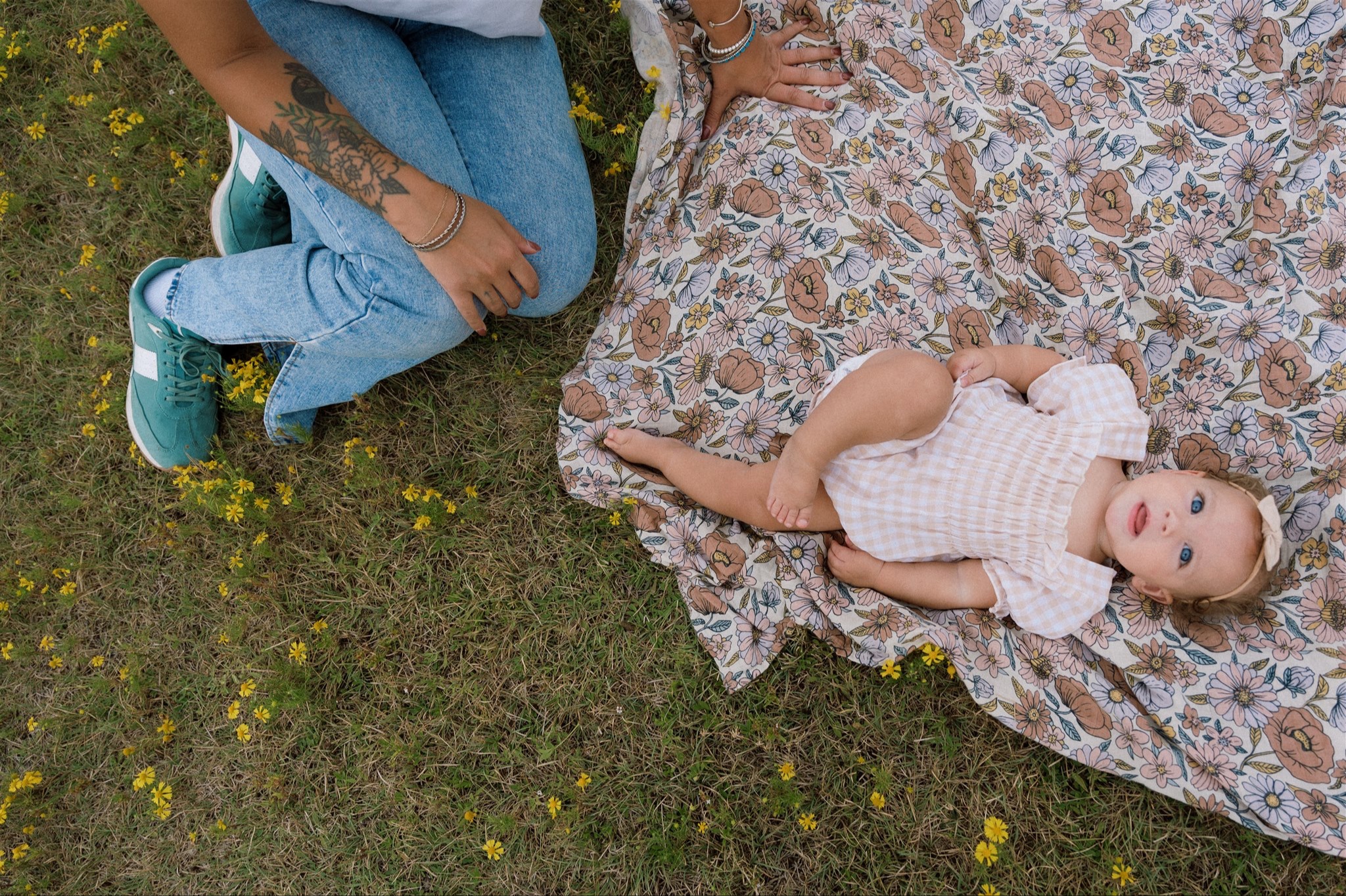 Parent sitting on the grass beside their baby on a floral blanket, capturing warmth and calm of holistic, family-centered pediatric care