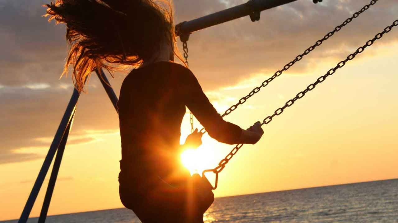 woman on a swingset looking toward an ocean sunset