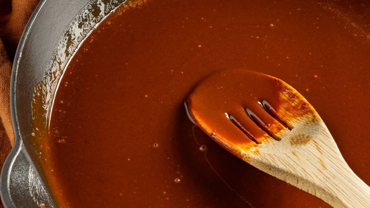 Homemade dark roux in cast iron skillet with wooden spoon, deep brown colora