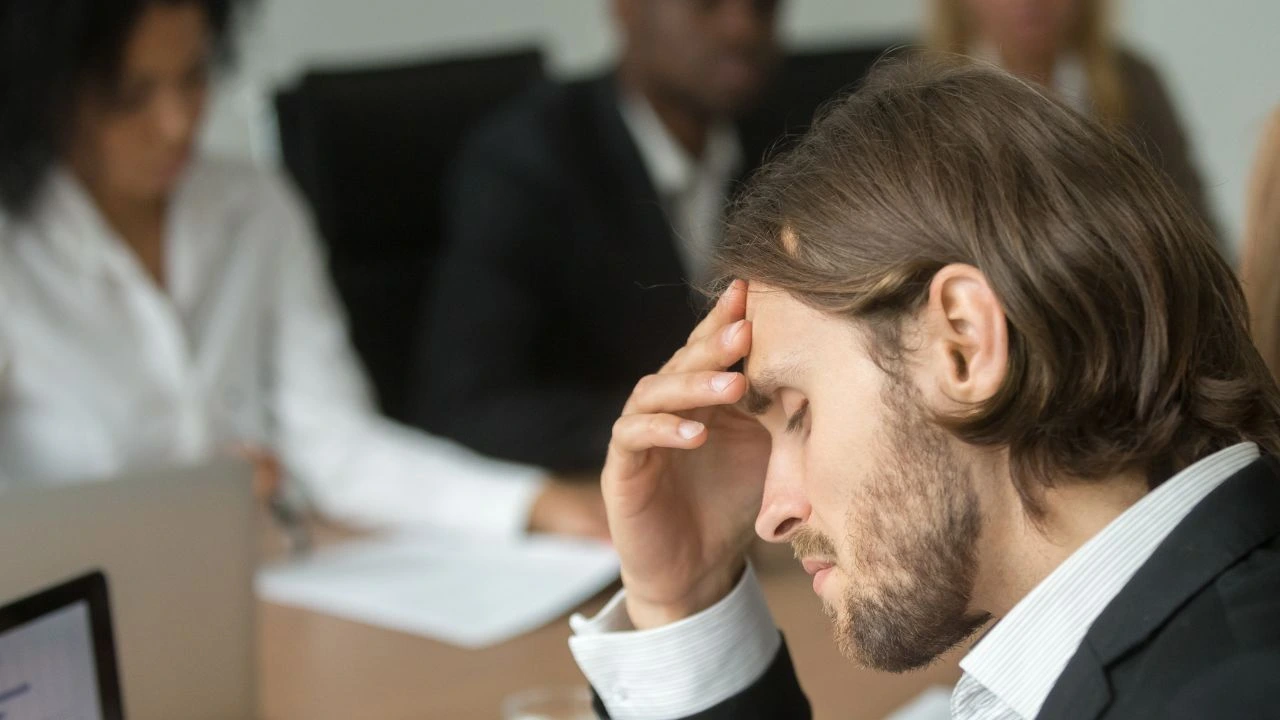 Frustrated tired businessman having strong headache at diverse team meeting due to fear 