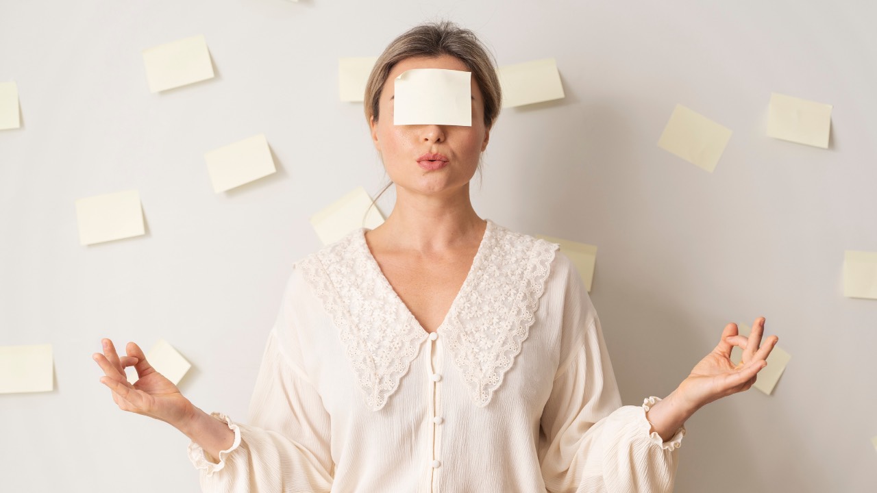 Woman with a sticky note covering her eyes, surrounded by notes on a wall, symbolizing leadership blind spots and lack of self-awareness.