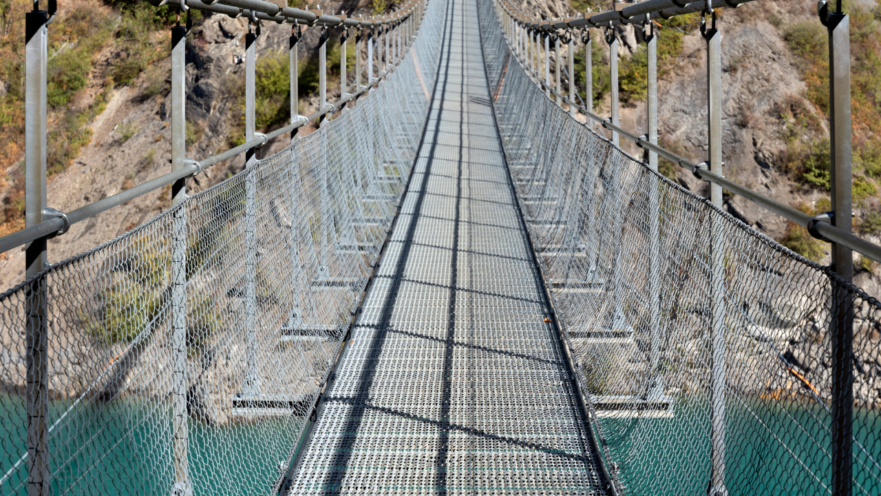 horizontal photograph of a modern glass suspension bridge stretching across a deep canyon This serves as a powerful metaphor for "structural trust" being the only thing that allows for progress over uncertain or dangerous terrain.