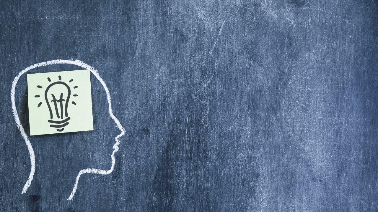 It visually Light bulb sticky note on the drawn face outline with chalk on blackboard represents "The Space to Think"