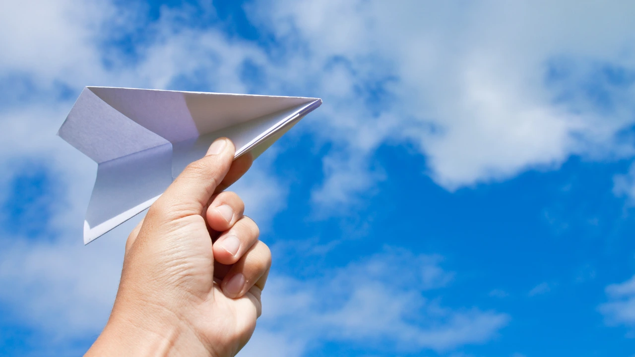 A leader’s hand releasing a paper airplane into the air, symbolising letting go of control and trusting the team to grow.