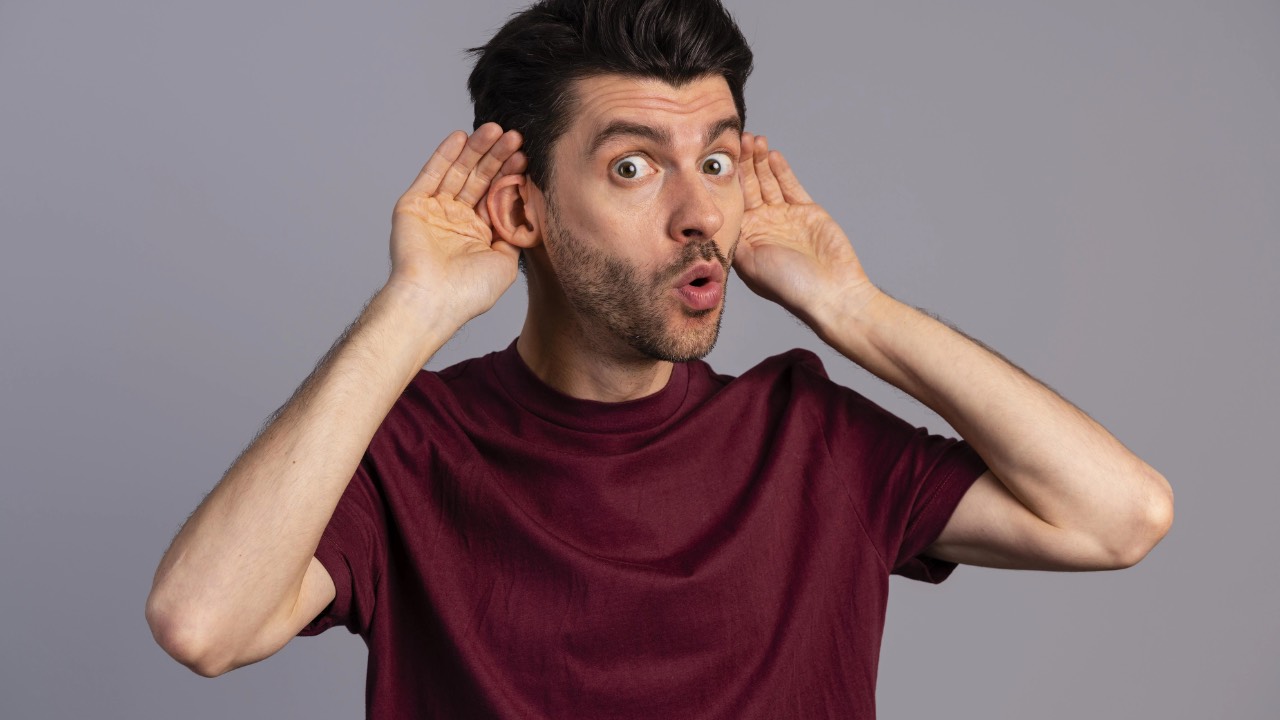 professional shirt cupping his ear with his hand, leaning forward slightly as if straining to hear a conversation or focusing intensely on listening.