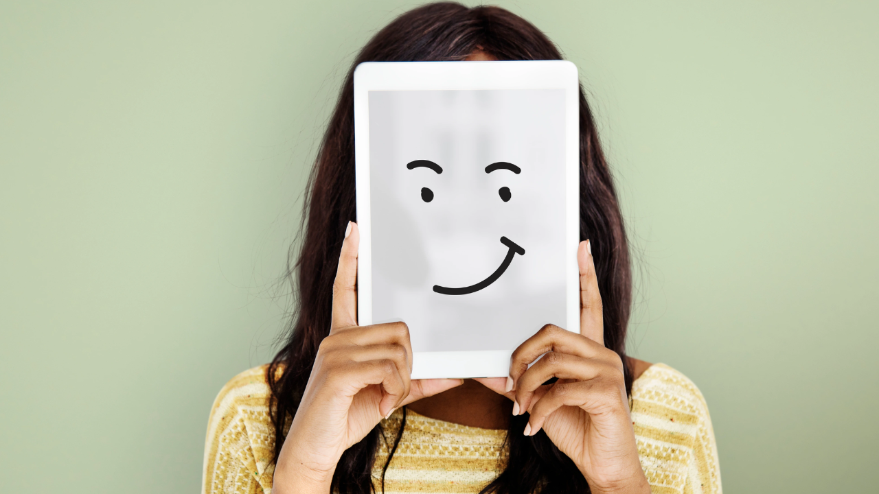 Person holding a tablet in front of their face showing a simple smiling face drawing, symbolizing hidden emotions and emotional expression.