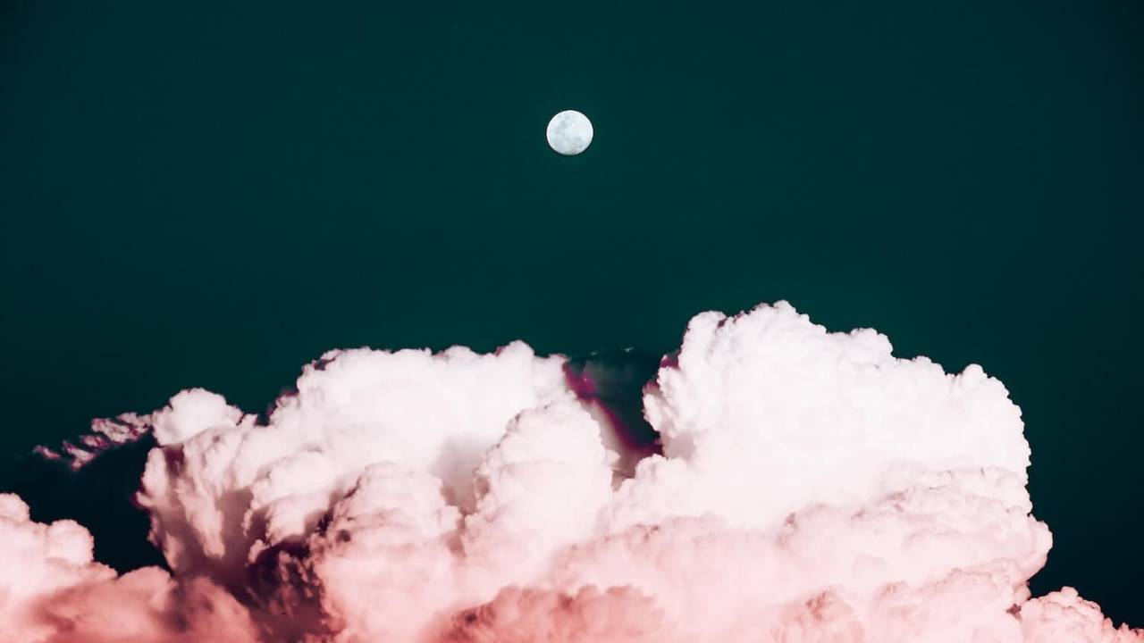 Photo of Fluffly Clouds Bursting Across a Navy Sky with a Full Moon