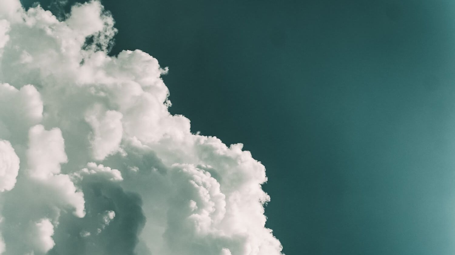 Photo of Fluffly Clouds Bursting Across a Teal Sky