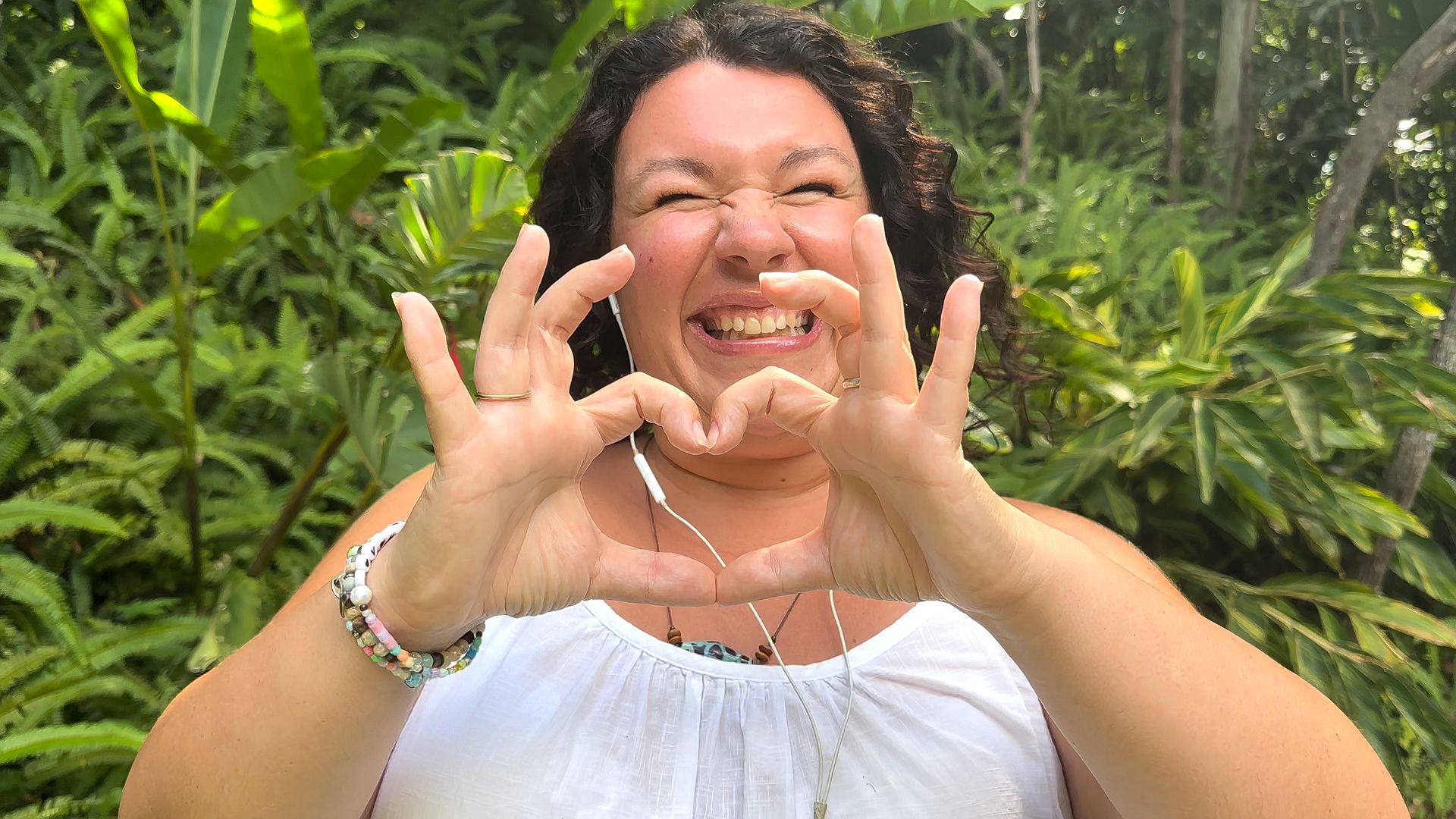 Natasha smiling and making a love heart gesture with her hands