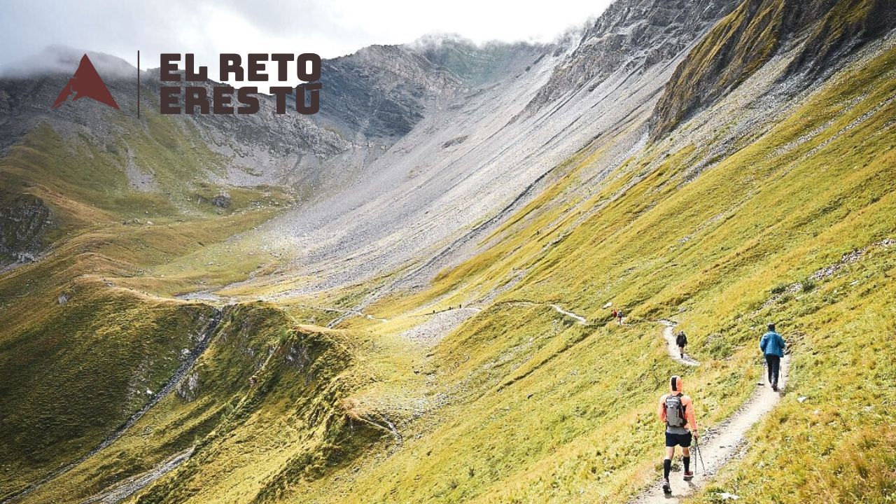 Tres corredores de ultra trail en sendero de montaña hacia valle alpino, simbolizando la longevidad deportiva y el juego infinito del trail running