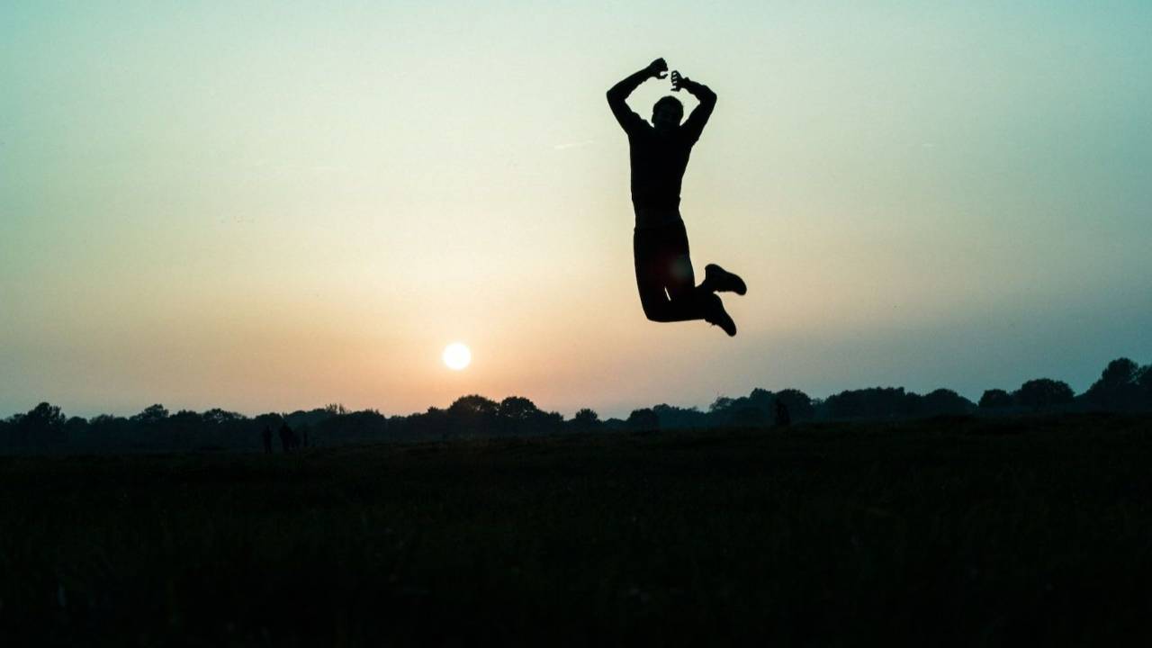 Uomo che ha ritrovato forza interiore salta sullo sfondo del tramonto