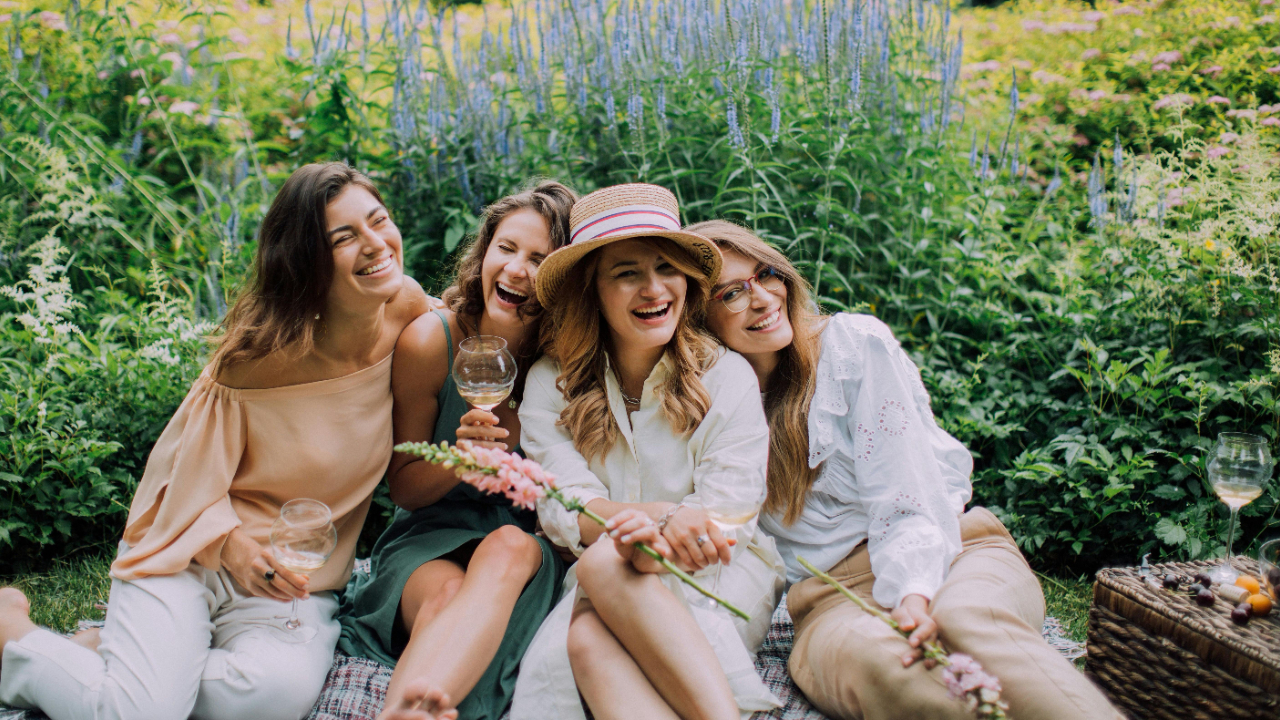 Four women laughing together in a garden setting, illustrating connection and the first signs of perimenopause.