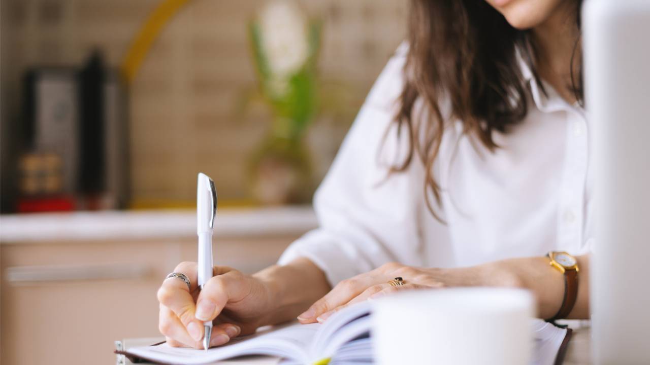 Woman gently writing in a journal at her kitchen table, starting to organize her finances with calm clarity.