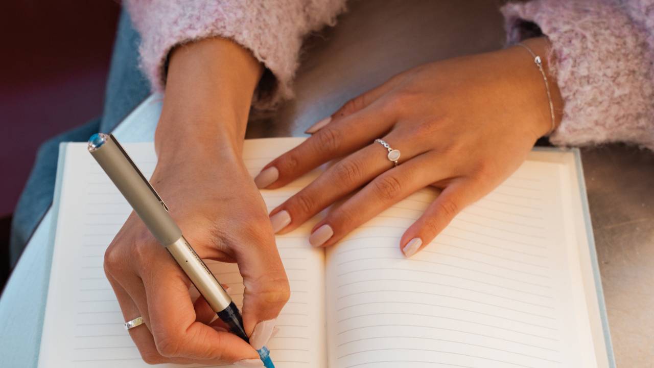 Woman journaling in a notebook with a pen, practicing gentle reflection and clarity during a quiet moment.