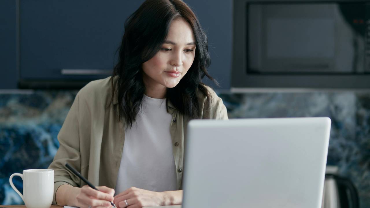 Woman calmly organizing bills at a kitchen table with a laptop and notebook, creating a simple, stress-free money routine