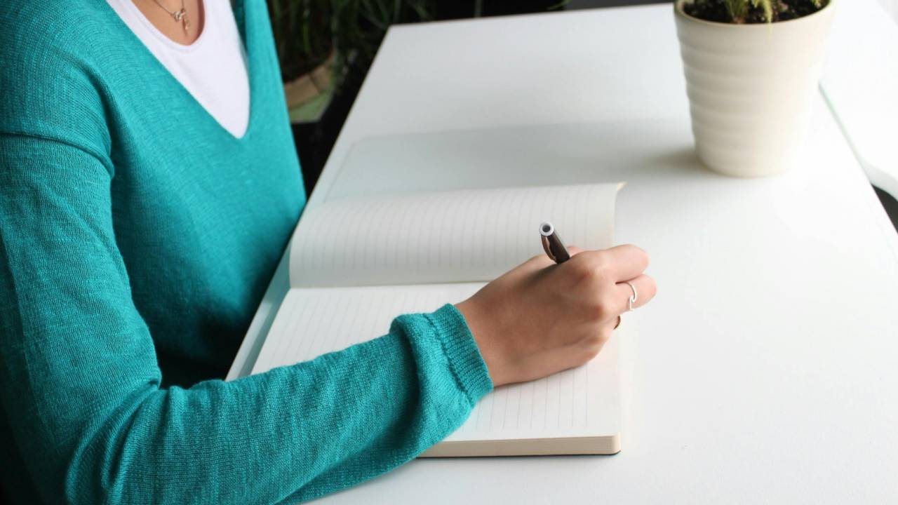 Woman writing in a notebook at a clean desk, creating a simple snapshot of her finances with calm focus and clarity