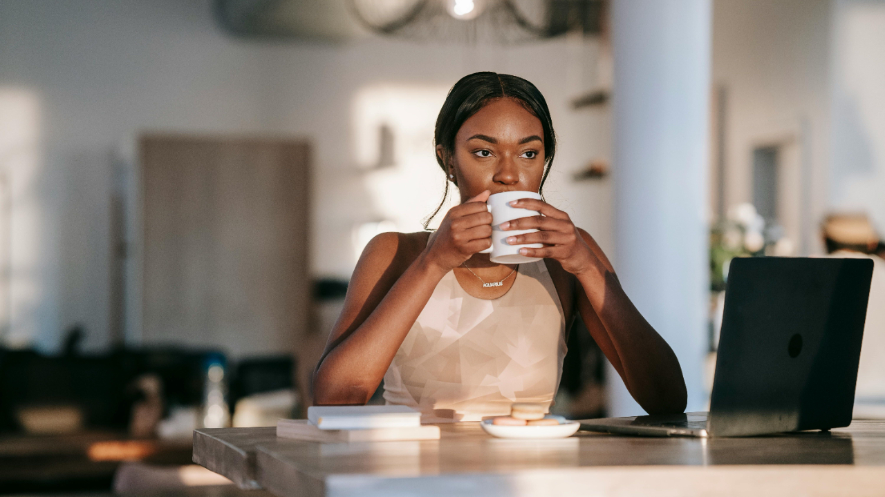 Woman sitting at a table with coffee and laptop in soft morning light, reflecting calmly while beginning a new financial chapter