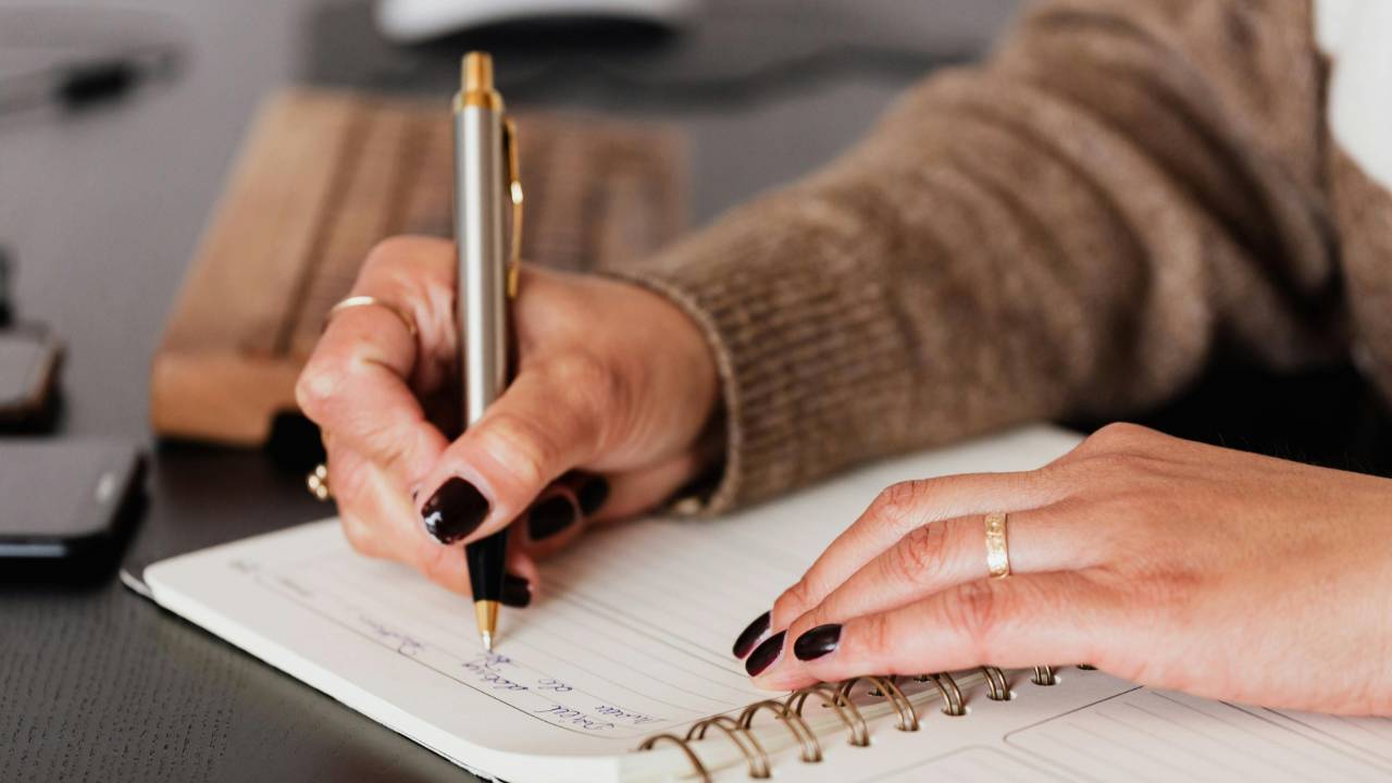 Close-up of a woman journaling in a notebook during a calm weekly clarity ritual, creating space to reflect, plan, and feel more confident with her finances.”