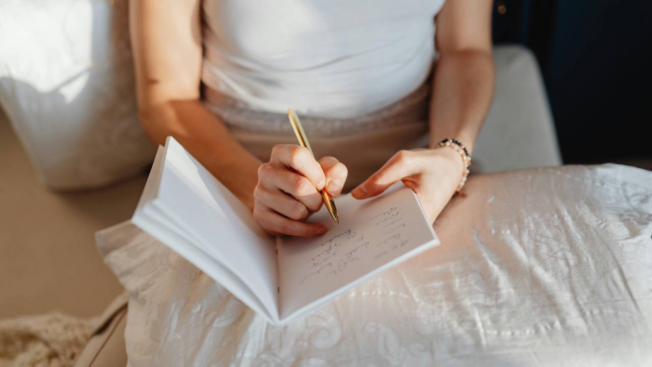 Woman journaling quietly on a bed in soft natural light, reflecting on emotions and personal thoughts about money and life.