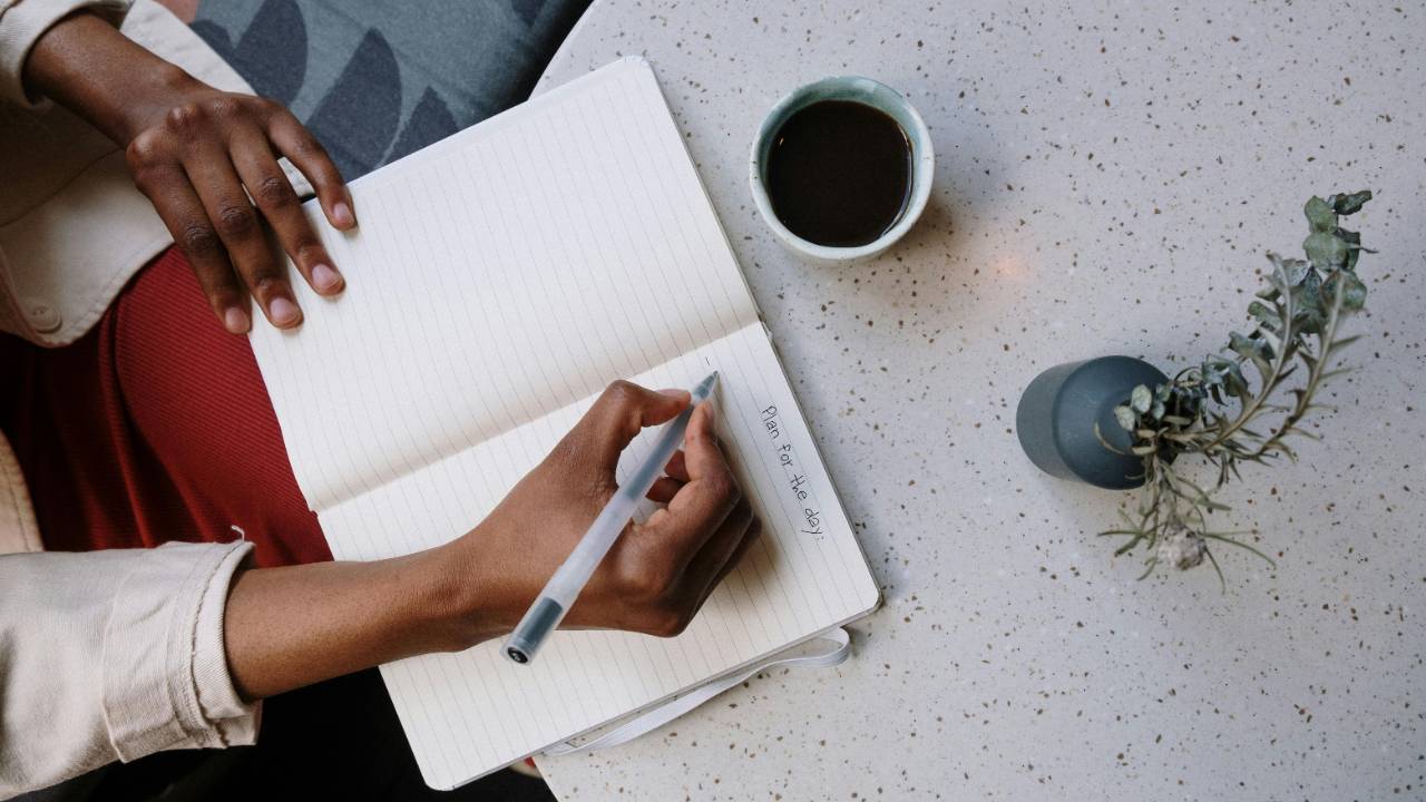 Woman journaling with a notebook and coffee, creating a simple spending plan for a fresh financial start
