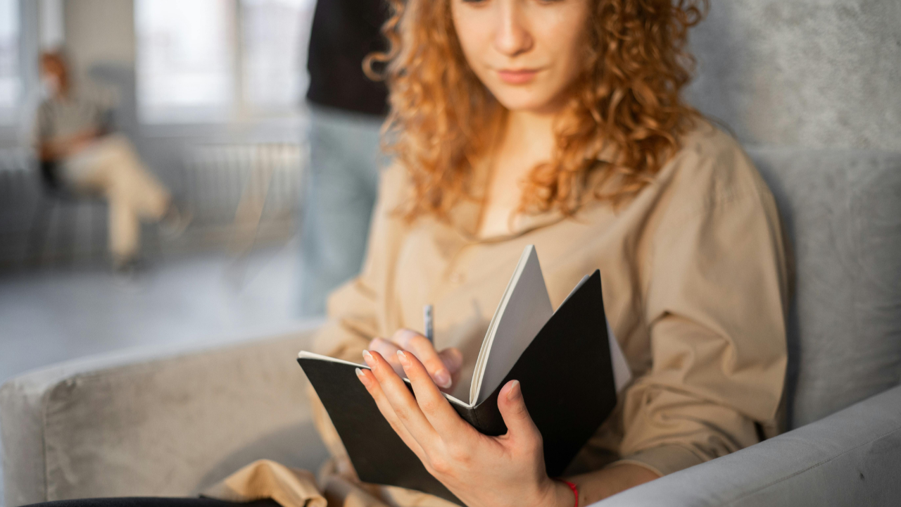 Woman journaling quietly on a couch, beginning to face her finances with honesty and calm