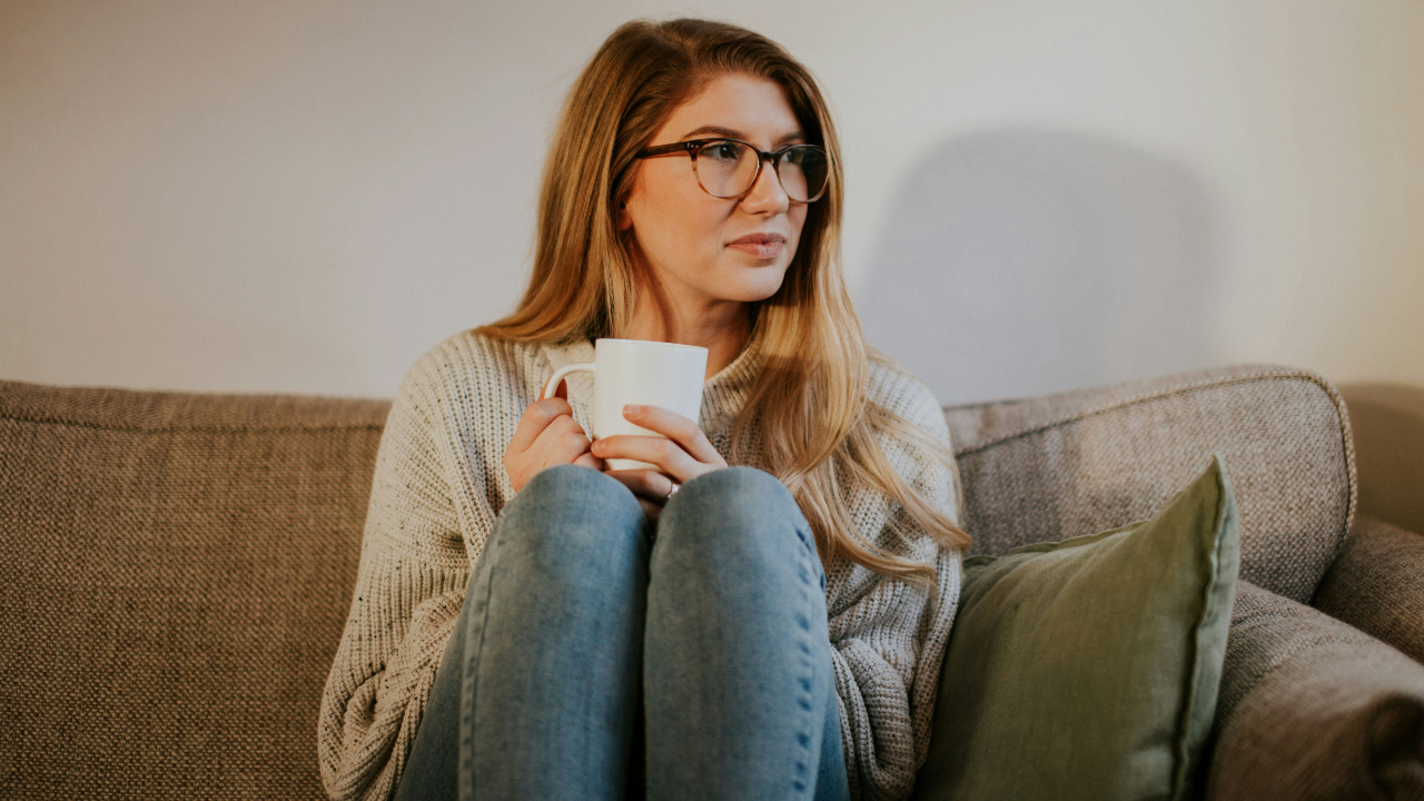 Woman sitting on a couch holding a coffee mug, reflecting quietly during a season of personal and financial growth
