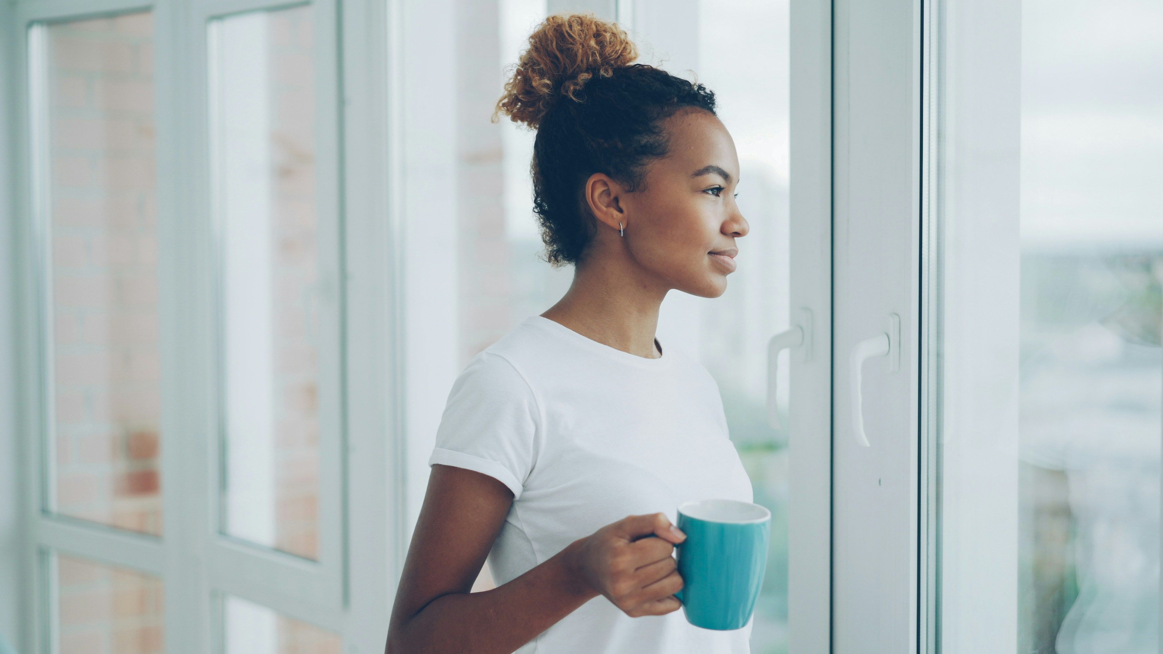 Woman holding a coffee mug while standing by a window, reflecting during a calm morning routine