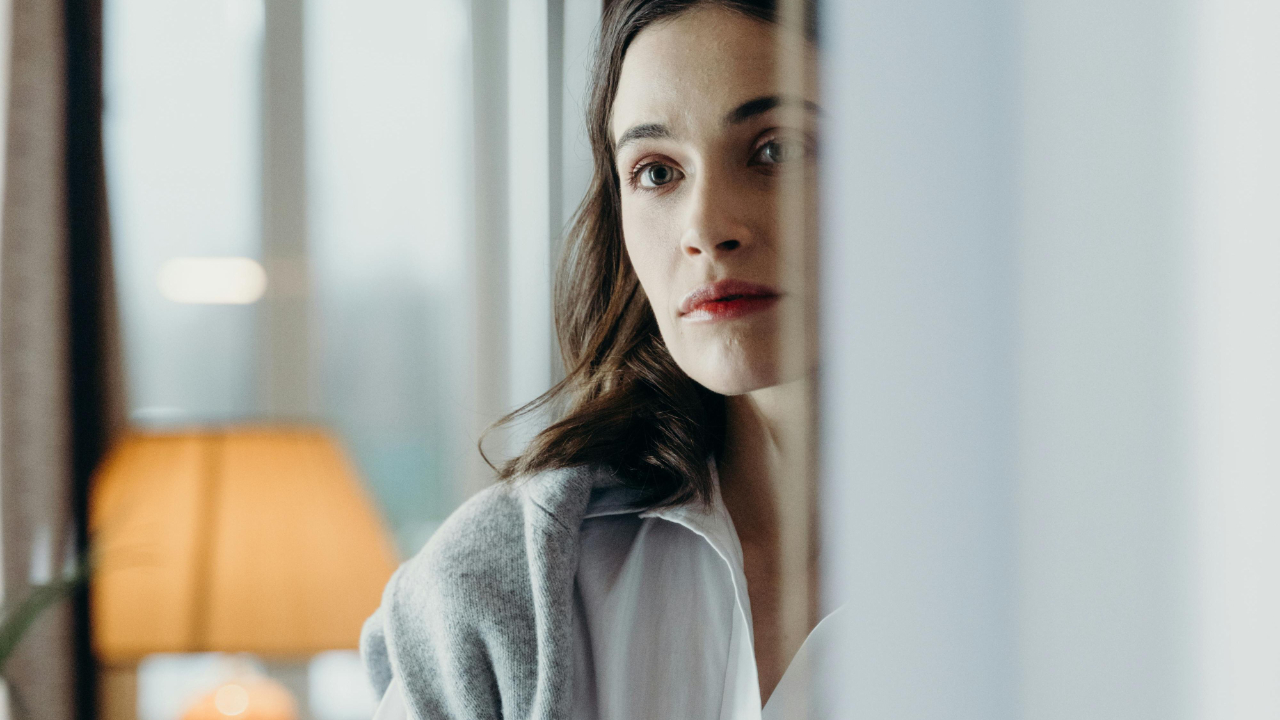Woman standing quietly with arms crossed, reflecting during a moment of financial avoidance and self-protection.