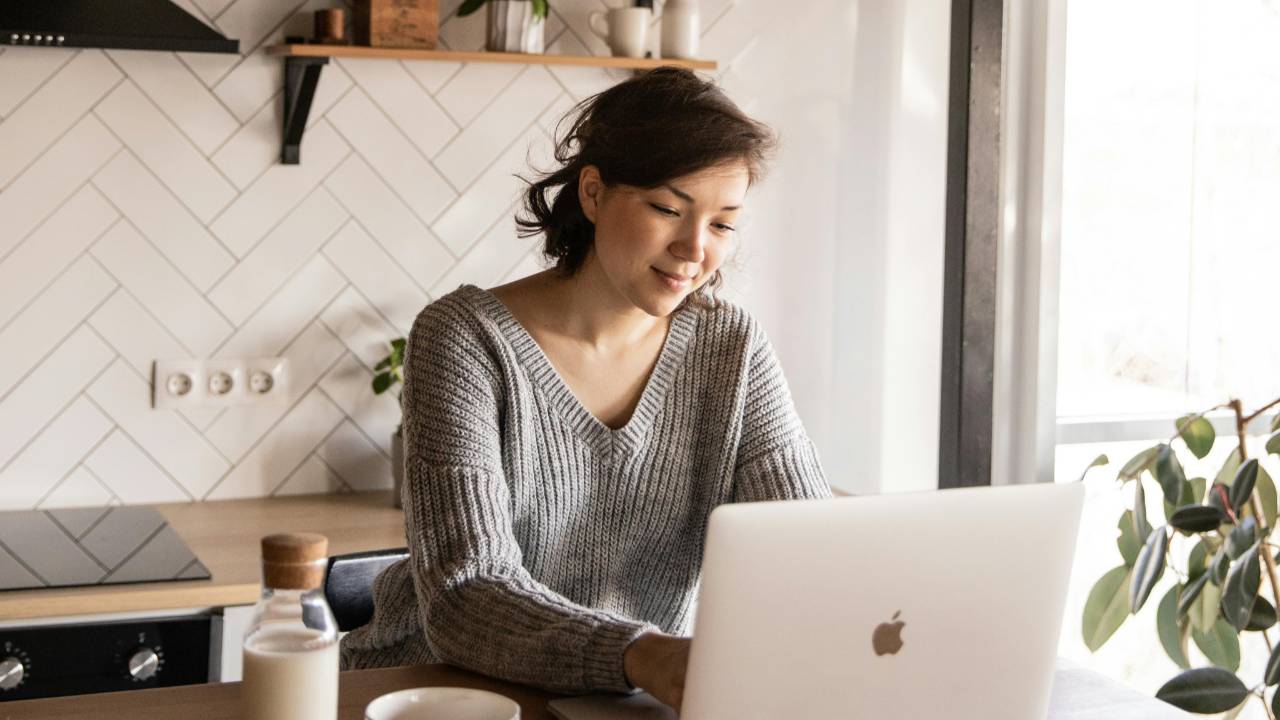 Woman sitting at a kitchen table with a laptop, calmly rebuilding her life and finances after a difficult turning point.
